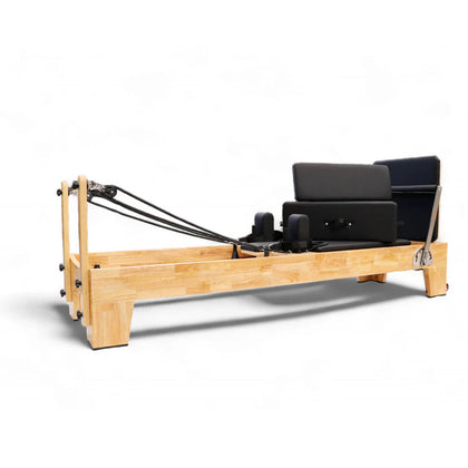 REFORMIA Oak Wood Pilates Reformer with Noir Black upholstery and solid oak frame, three-quarter studio view